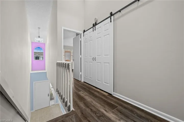 Hall with an upstairs landing, a barn door, wood finished floors, a towering ceiling, and a chandelier