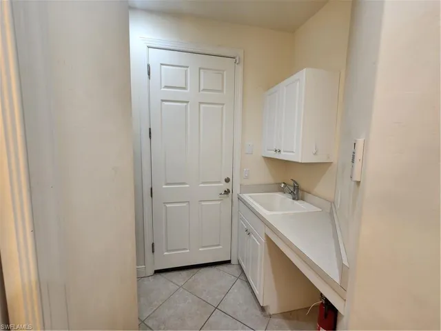 Clothes washing area featuring light tile patterned floors and a sink. Powder Room to left side of entry.