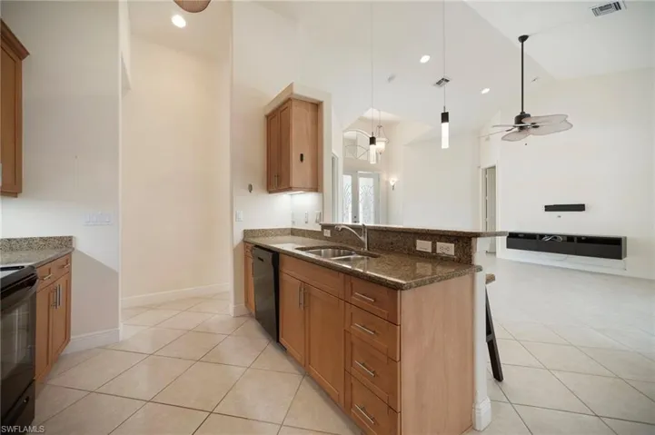 Kitchen with black appliances, a sink, dark stone counters, a breakfast bar area, and light tile patterned floors