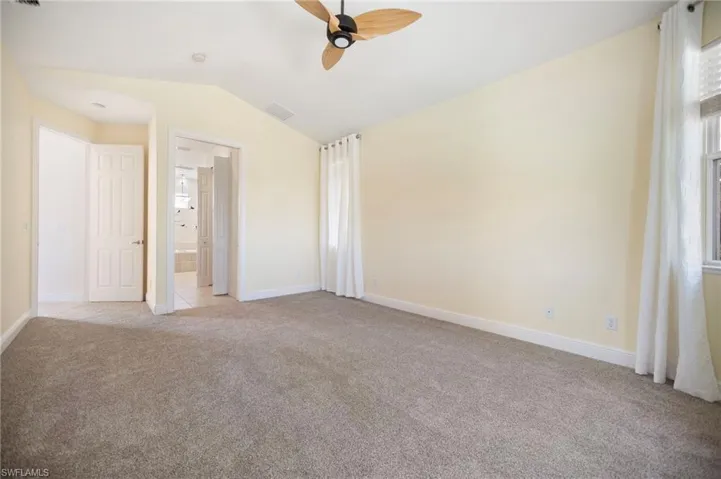 Primary bedroom with lofted ceiling, baseboards, visible vents, and light carpet
