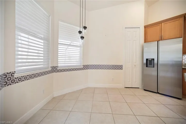 Kitchen with brown cabinets, stainless steel fridge with ice dispenser, light tile patterned floors, baseboards, and vaulted ceiling
