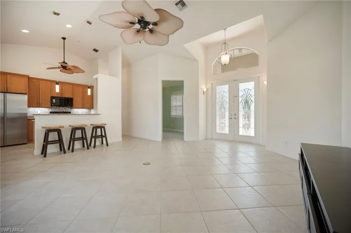 Kitchen with visible vents, stainless steel refrigerator, brown cabinetry, black microwave, and ceiling fan. Office/Den entry next to main entry.