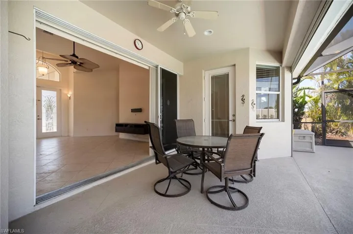 View of patio with outdoor dining space, glass enclosure, and a ceiling fan