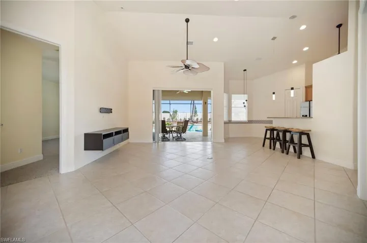 Unfurnished living room with light tile patterned flooring, recessed lighting, ceiling fan, and a towering ceiling. Primary suite left side.
