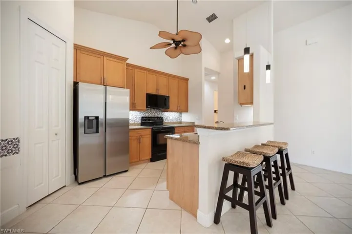 Kitchen featuring stone countertops, black appliances, light tile patterned flooring, and a ceiling fan