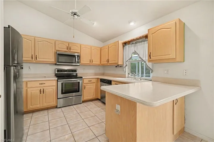 Kitchen featuring a vaulted ceiling with a ceiling fan, light wood-finish cabinetry, stainless steel appliances, and tile flooring
