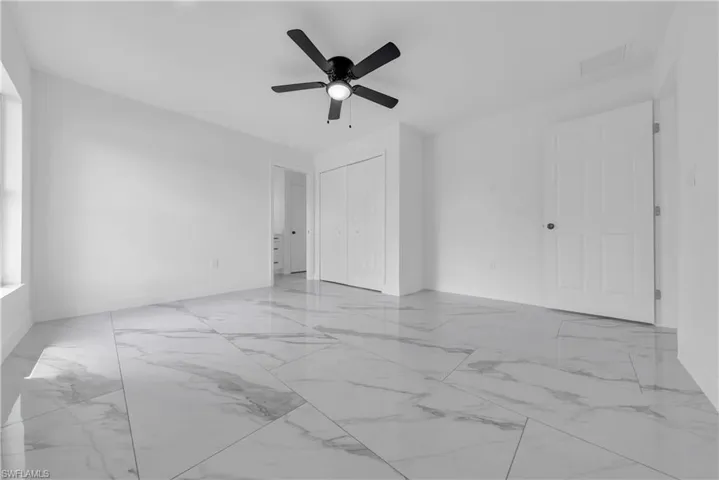 Unfurnished bedroom featuring light marble finish floors, ceiling fan, and a closet