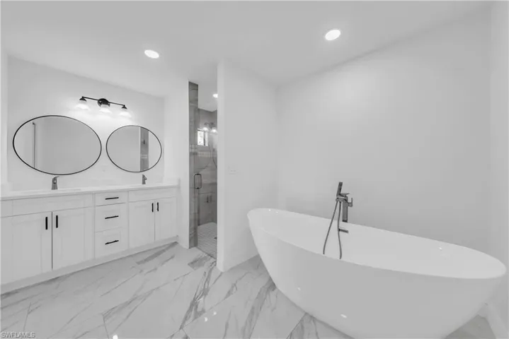 Full bath featuring a freestanding tub, double vanity, a stall shower, recessed lighting, and light marble finish flooring