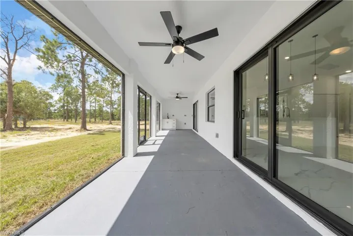 Unfurnished sunroom with ceiling fan, a patio, concrete flooring, and plenty of natural light