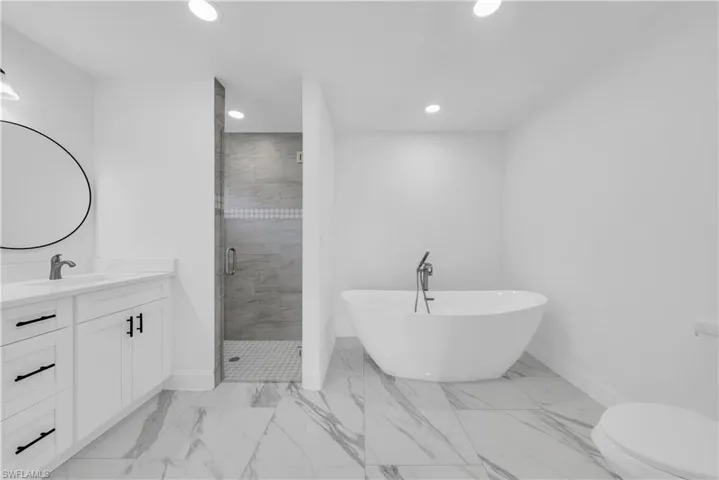 Full bathroom with vanity, a freestanding tub, a stall shower, and recessed lighting