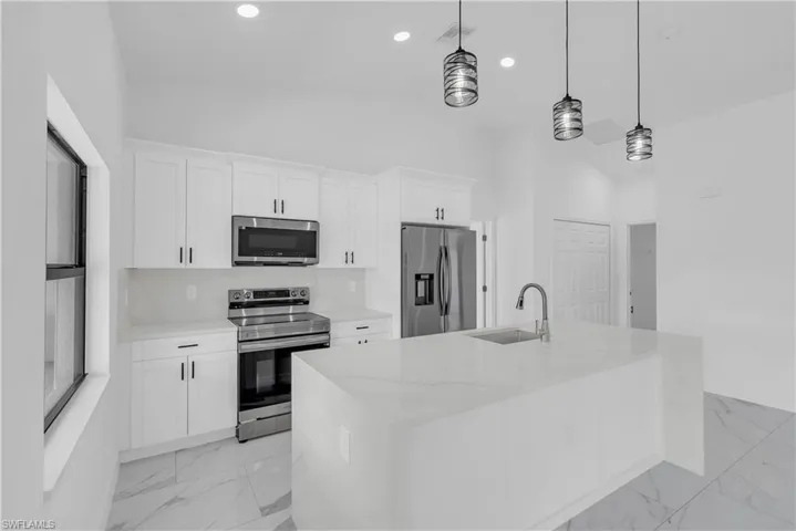 Kitchen featuring stainless steel appliances, hanging light fixtures, white cabinetry, light stone countertops, and recessed lighting