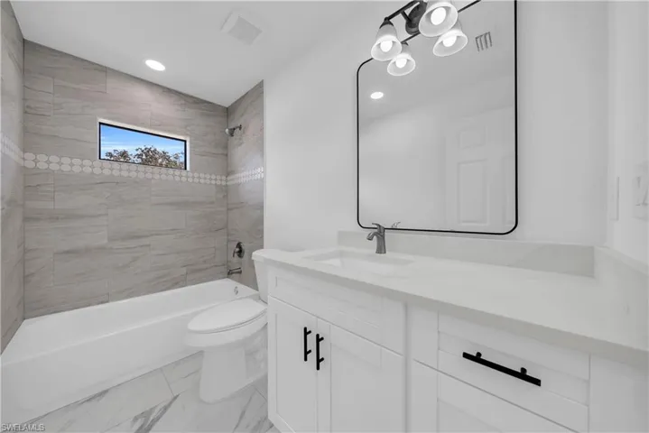 Bathroom featuring bathtub / shower combination, vanity, recessed lighting, and light marble finish flooring