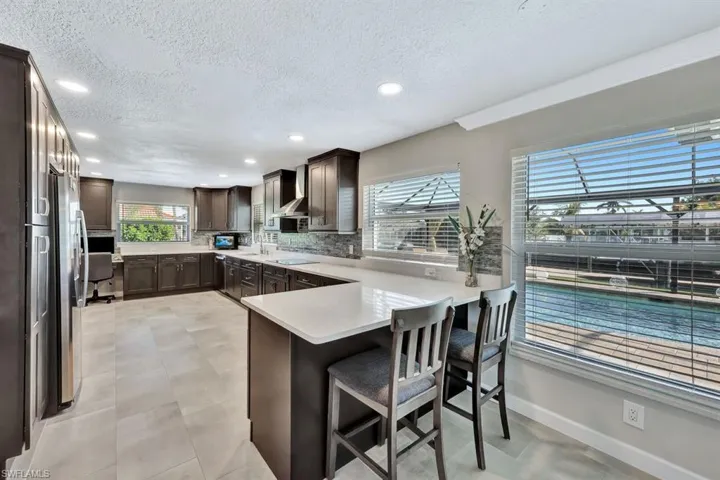 Kitchen with a breakfast bar, a textured ceiling, black electric cooktop, decorative backsplash, and kitchen peninsula
