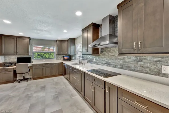 Kitchen with sink, tasteful backsplash, built in desk, black electric cooktop, and wall chimney exhaust hood