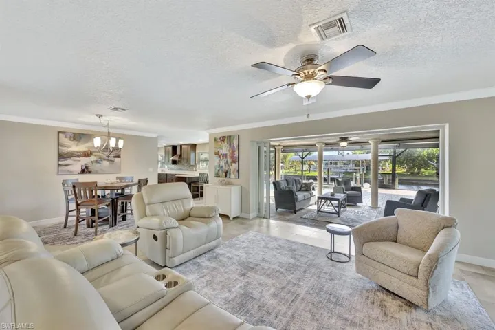 Tiled living room with crown molding, ceiling fan with notable chandelier, and a textured ceiling