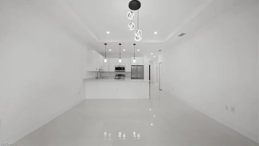 Kitchen with stainless steel appliances, a raised ceiling, a peninsula, white cabinets, and light countertops