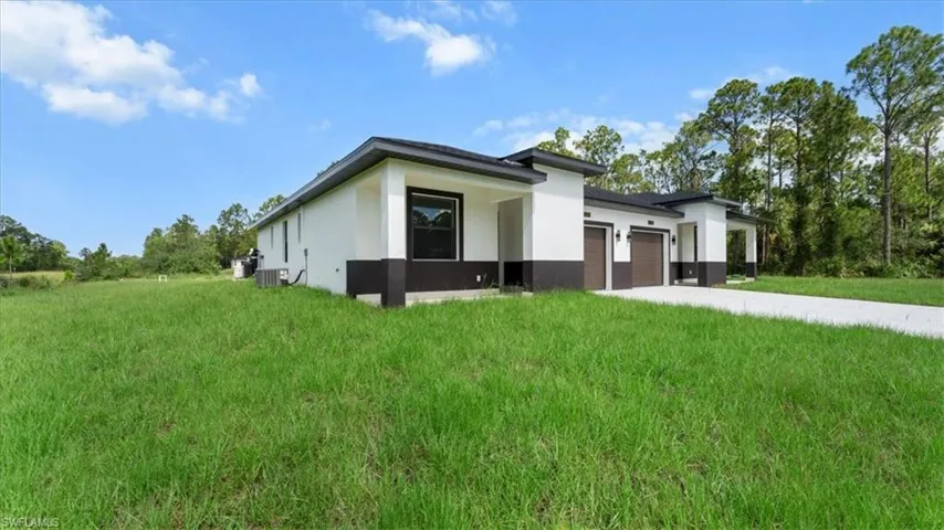 View of side of home with stucco siding, an attached garage, driveway, and a yard
