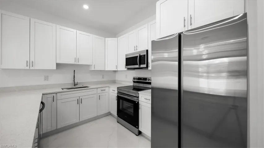 Kitchen with stainless steel appliances, light marble finish flooring, white cabinets, light countertops, and recessed lighting