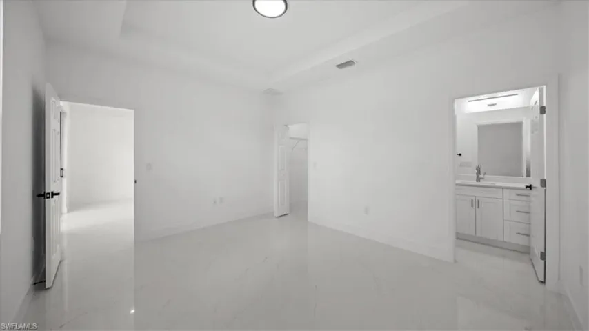 Unfurnished bedroom featuring light marble finish flooring, connected bathroom, a raised ceiling, and a spacious closet