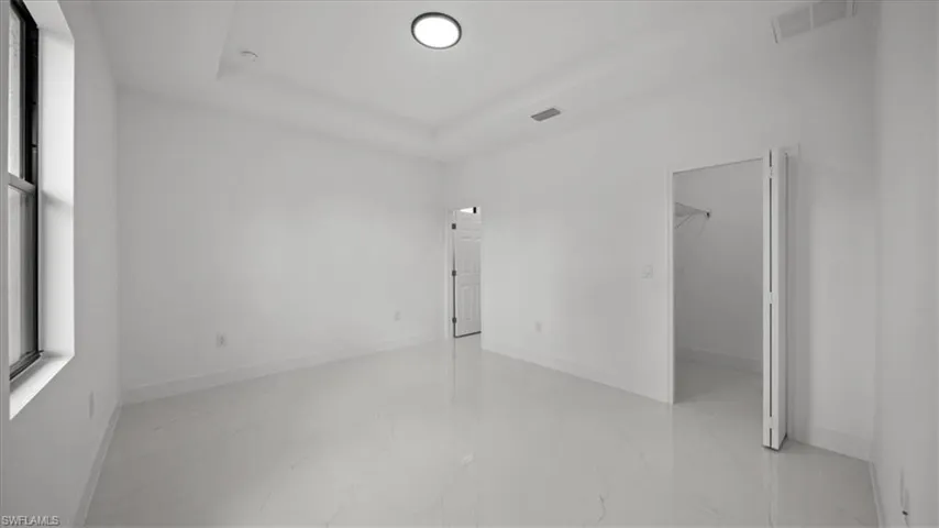 Unfurnished bedroom with marble finish floors, a spacious closet, and a tray ceiling