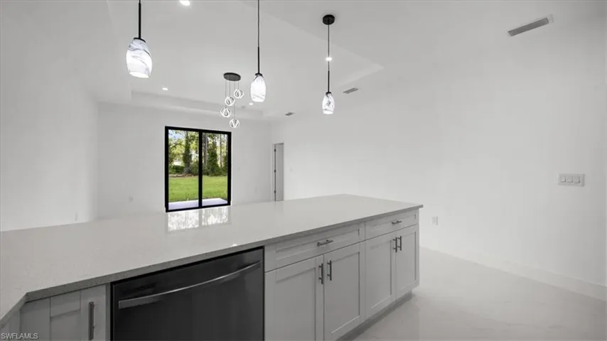 Kitchen featuring a raised ceiling, dishwashing machine, light countertops, hanging light fixtures, and light marble finish floors