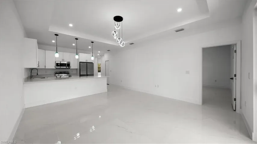 Unfurnished living room with a raised ceiling, recessed lighting, and light marble finish floors