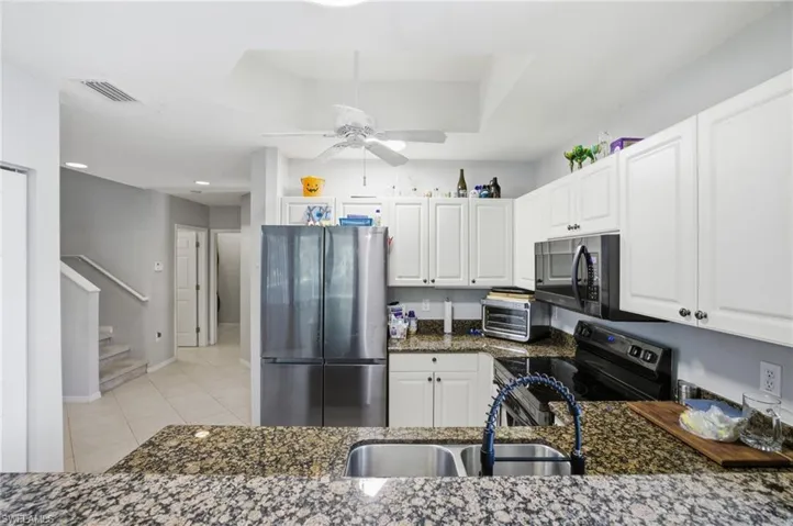 Kitchen featuring stainless steel appliances, white cabinetry, dark stone countertops, ceiling fan, and light tile patterned floors
