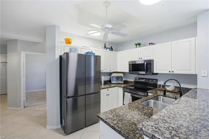 Kitchen with stainless steel appliances, dark stone counters, white cabinets, and a ceiling fan
