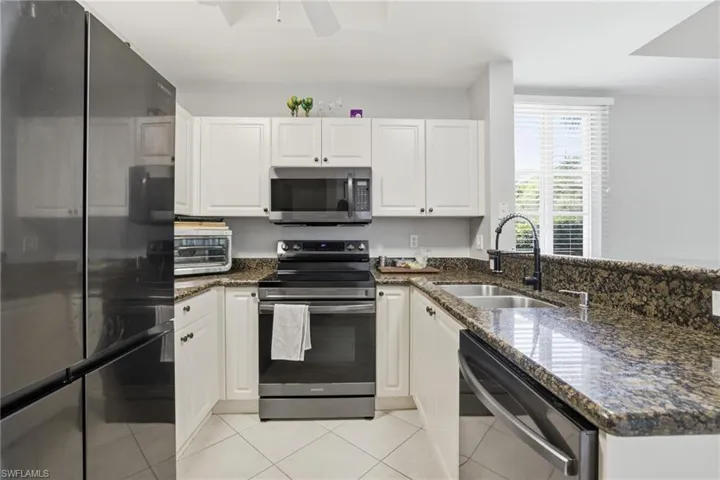 Kitchen featuring appliances with stainless steel finishes, dark stone countertops, white cabinetry, and a peninsula
