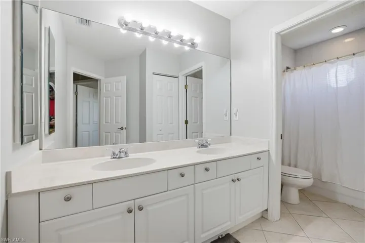 Bathroom with double vanity, light tile patterned floors, and shower / bath combo with shower curtain