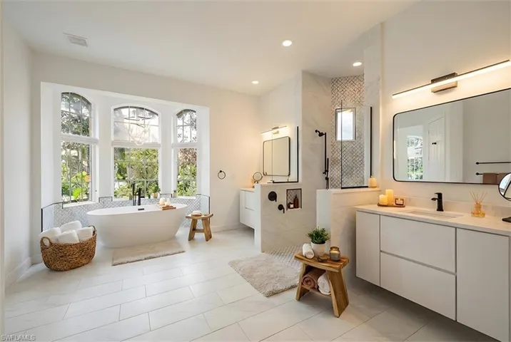 Bathroom featuring a walk in shower, two vanities, recessed lighting, a freestanding tub, and light tile patterned floors