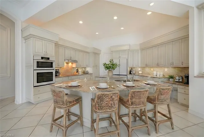 Kitchen featuring a kitchen bar, light stone countertops, double wall oven, an island with sink, and ornamental molding