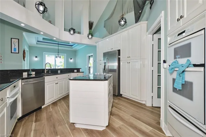 Kitchen with stainless steel appliances, a warming drawer, white cabinetry, dark stone counters, and light wood-type flooring