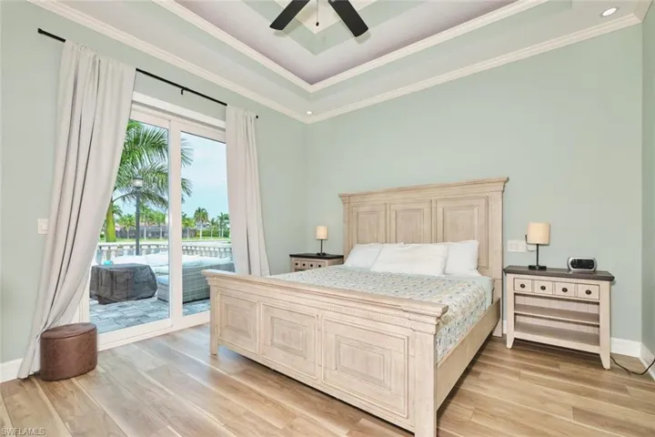 Bedroom featuring a raised ceiling, light wood-style flooring, access to exterior, ceiling fan, and crown molding