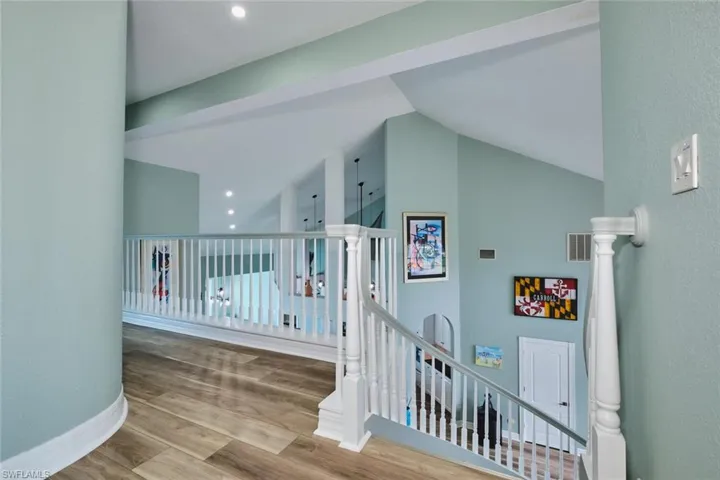 Hallway featuring an upstairs landing, light wood-type flooring, a textured wall, and high vaulted ceiling