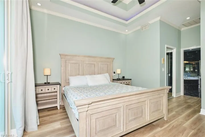 Bedroom with light wood finished floors, crown molding, recessed lighting, ceiling fan, and a tray ceiling