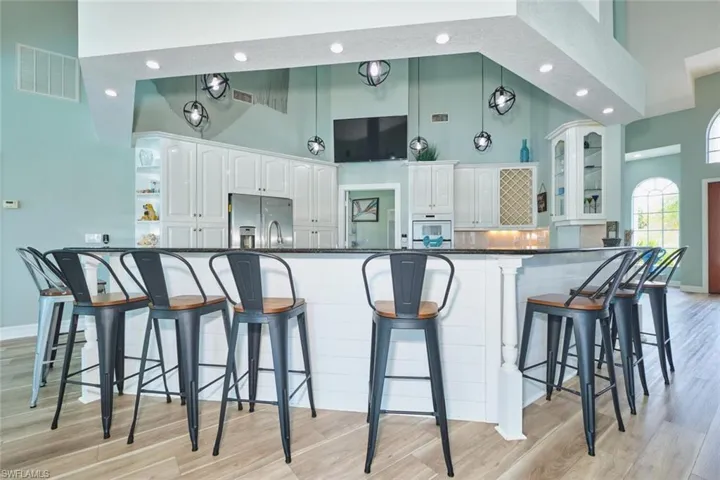 Kitchen with a kitchen breakfast bar, a high ceiling, white cabinetry, stainless steel fridge, and recessed lighting