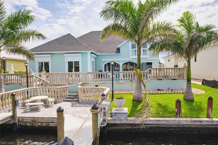 Back of house with a shingled roof, a patio area, stucco siding, and a water view