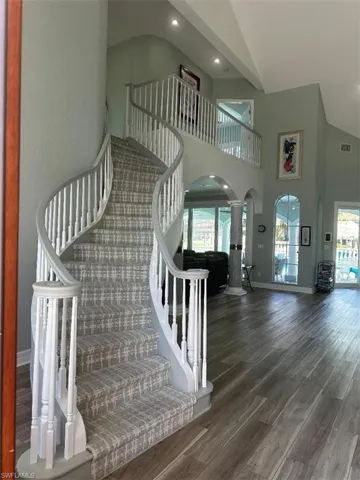 Staircase with wood finished floors, recessed lighting, and high vaulted ceiling