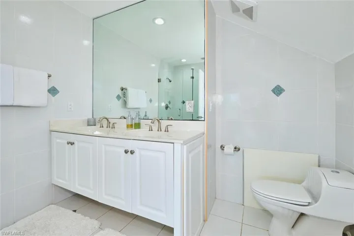 Bathroom featuring tile walls, light tile patterned floors, double vanity, a shower stall, and recessed lighting