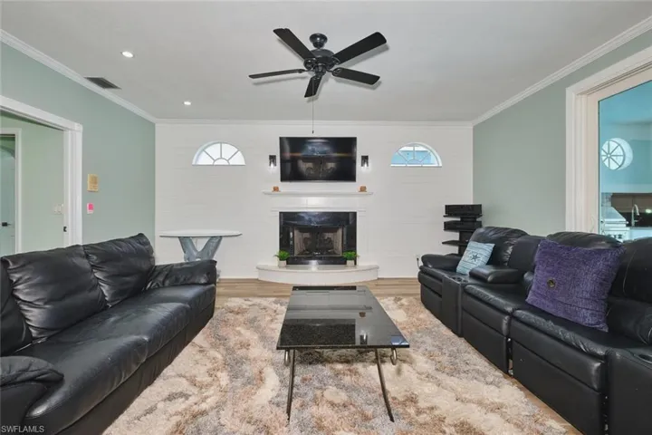 Living room featuring ornamental molding, a fireplace, ceiling fan, wood finished floors, and recessed lighting