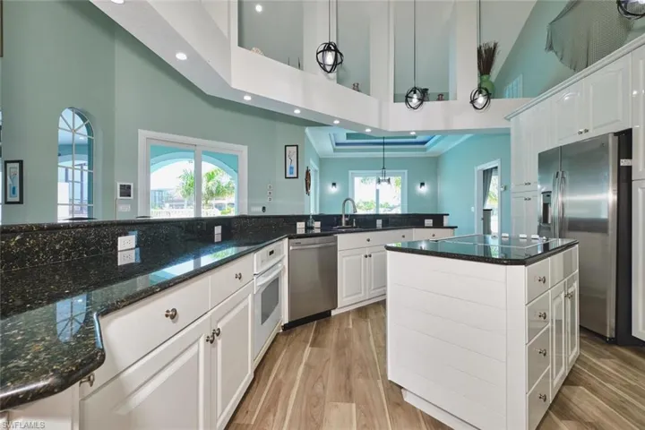 Kitchen with white cabinets, dark stone countertops, appliances with stainless steel finishes, light wood finished floors, and recessed lighting
