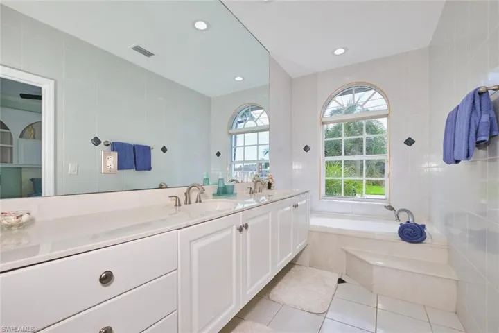 Bathroom featuring tile walls, a bath, double vanity, light tile patterned floors, and recessed lighting