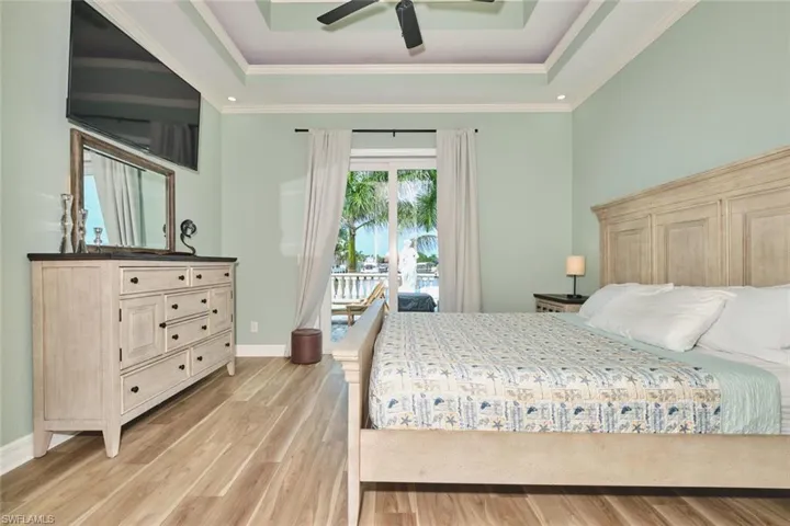 Bedroom featuring a tray ceiling, access to exterior, light wood finished floors, a ceiling fan, and crown molding