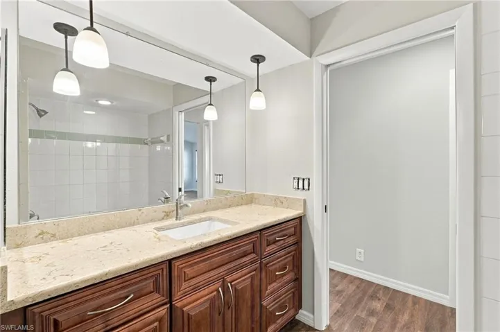 Vanity featuring a stone-composite countertop, undermount sink, shaker-style wooden cabinetry, polished metal hardware, and three pendant lights