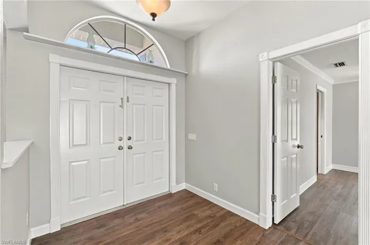 Double-door entryway featuring an arched transom window, wood-finish flooring, crisp white trim, and a neutral color palette