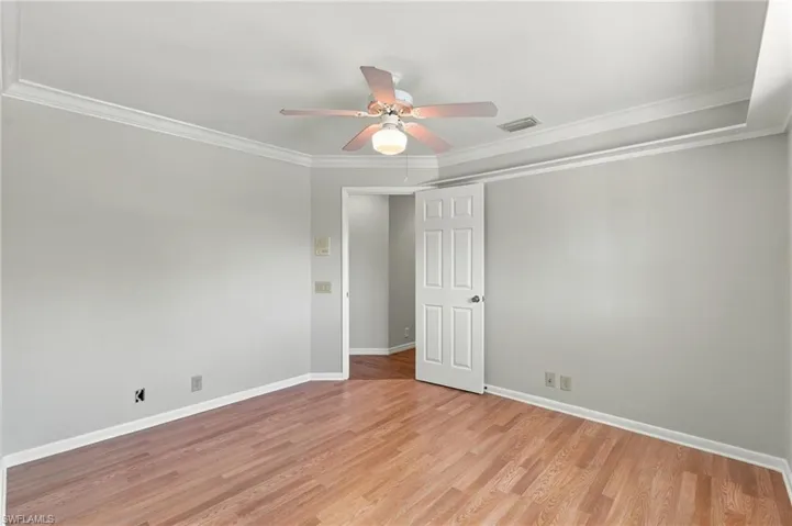 Room featuring tray ceilings, wood-finish flooring, and a central ceiling fan with integrated lighting
