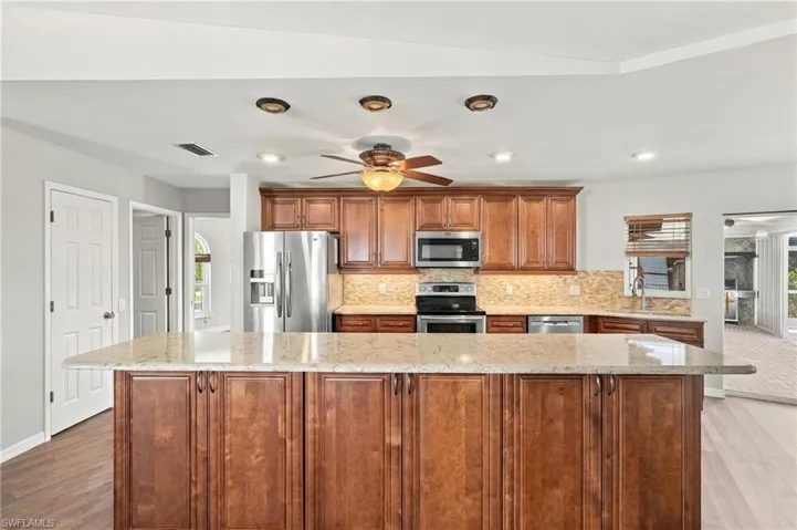 Kitchen featuring wood cabinetry, stone-finish countertops, stainless steel appliances, a center island, and recessed lighting