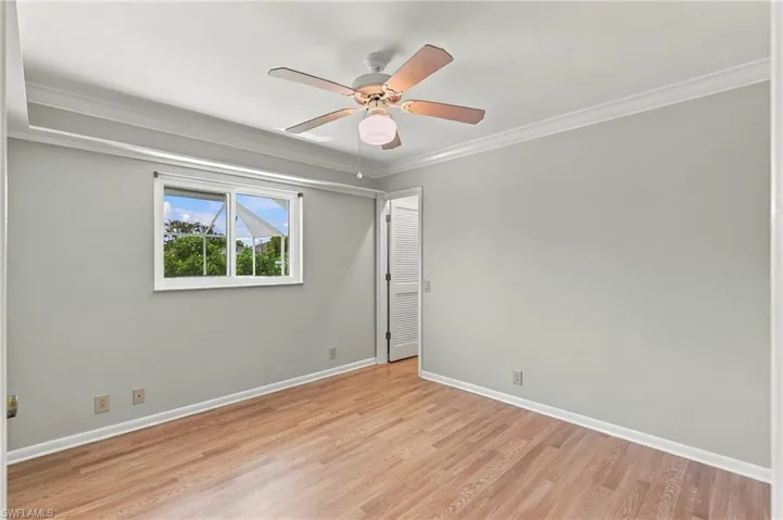 Room featuring wood-finish flooring, crown molding, a ceiling fan with integrated lighting, and a horizontal sliding window