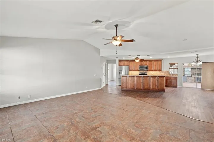 Open floor plan featuring vaulted ceilings, tile flooring, wood-finish cabinetry, built-in stainless steel appliances, and wood-finish flooring